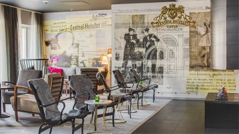 Hotell lobby med bord, stolar, kamin och ett konstverks om fondvägg
