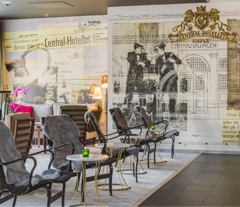 Hotell lobby med bord, stolar, kamin och ett konstverks om fondvägg
