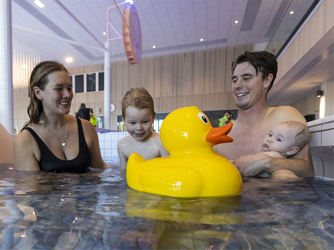 Two adults and two children in a pool,, a yellow bathing duck in the front .