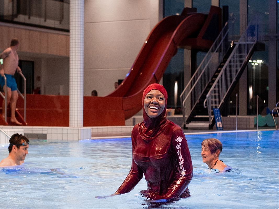 A woman in a burkini, in the background a red slide.