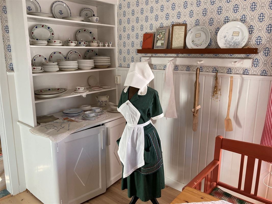 Ett köksskåp med porslin och en docka ståendes framför. 