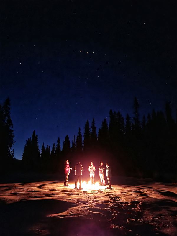 Fem människor som står i mörkret runt en eld. 