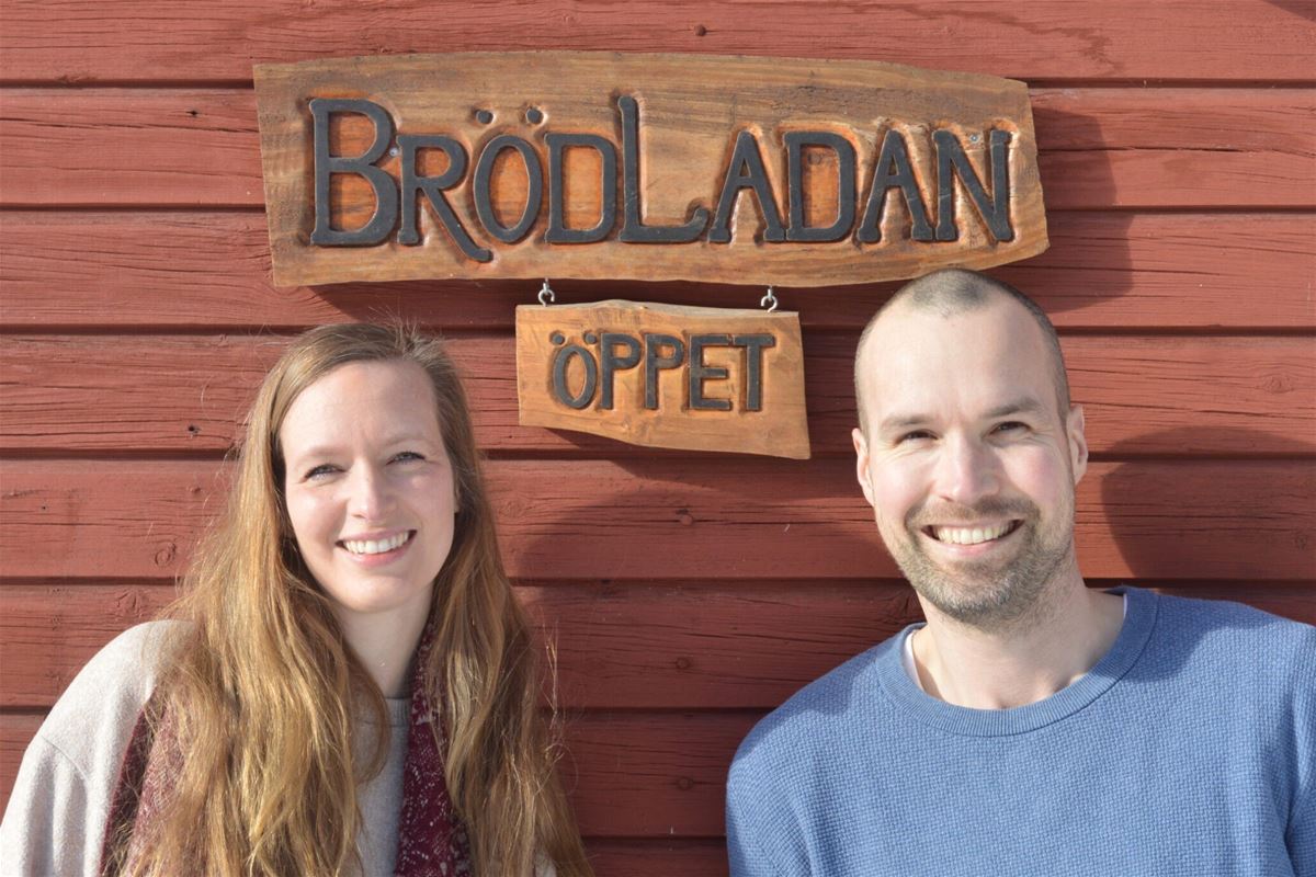 Fota av ägarna Marye och Rens mot husväggen med en träsnidad skylt med logo för Brödladan.
