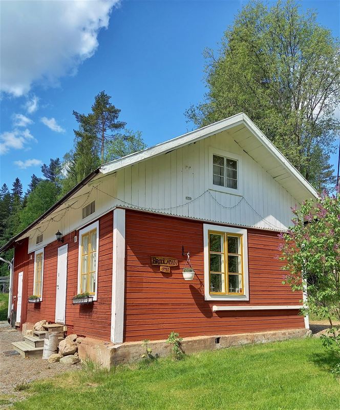 Exteriör av huset med rött timmer på nedre delen och vit del under taket.