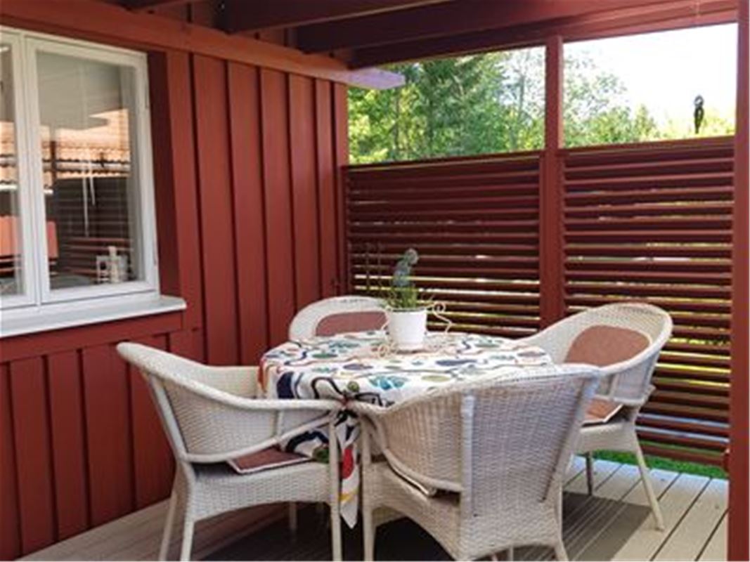 Sittgrupp med bord och fåtöljer på inglasad veranda.