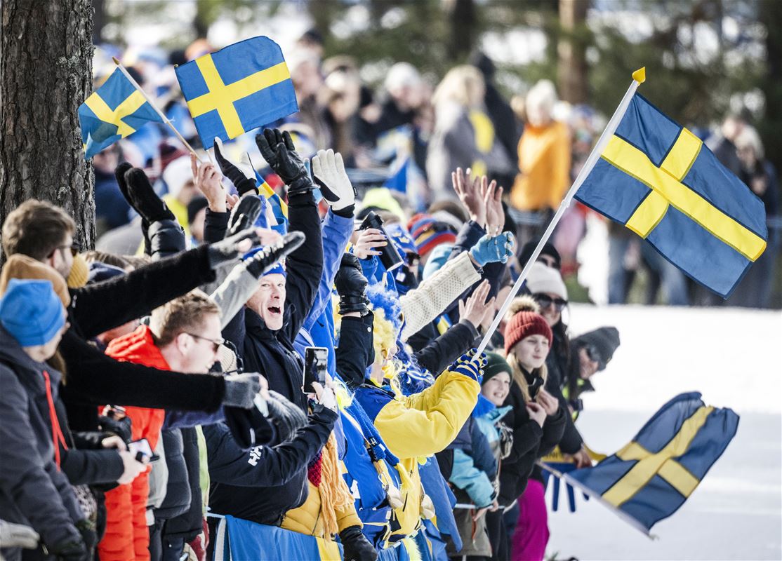 Publik som står längs spåret och viftar med svenska flaggor.