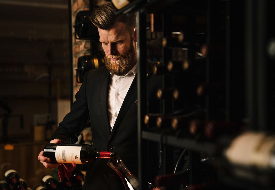 En man i svart kavaj och vit skjorta håller i en flaska rödvin. 