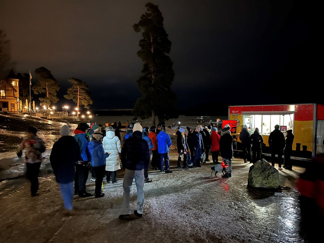 Människor på isen, försäljning i en kiosk, ljussken och en byggnad i bakgrunden.
