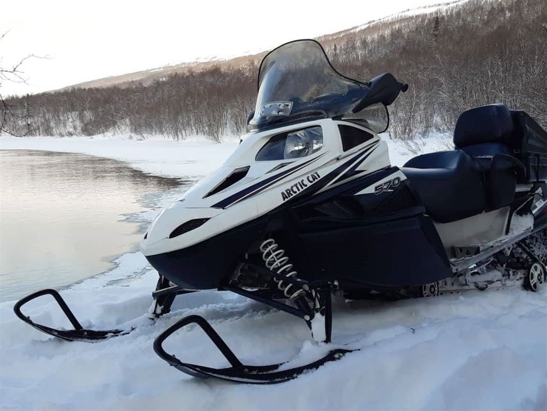 Snowmobile, lake, forest and mountains in the background.