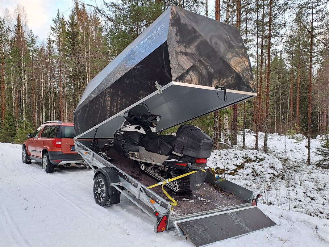 A snowmobile trailer, a car, forest in the background.