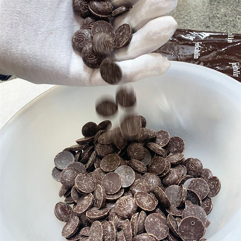 Chokladpraliner faller ur en hand ned i en vit skål.