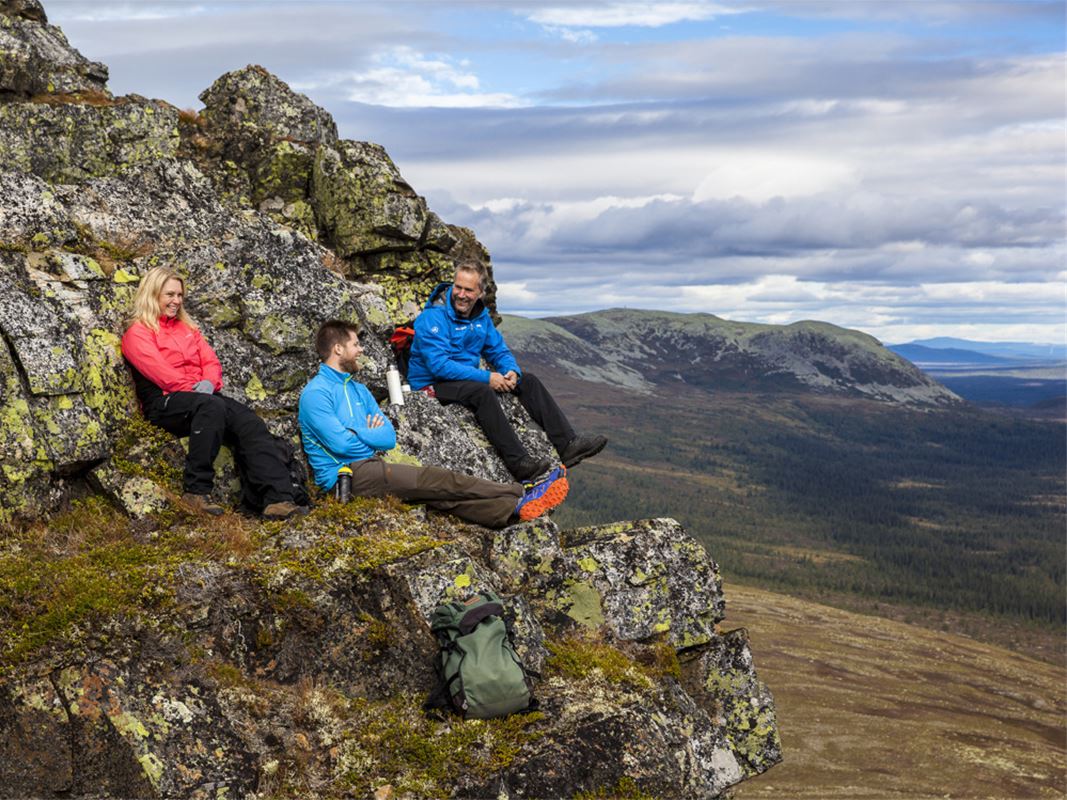 Tre personser sitter på en bergssluttning och tittar på utsikten.