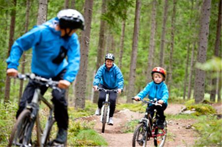 Två vuxna och ett barn i blåa kläder cyklar på stig.