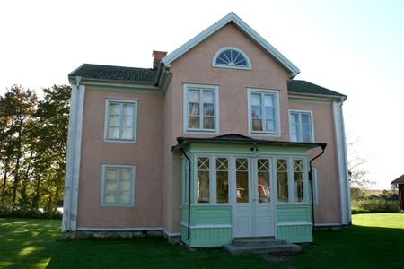 En tvåvåningsbyggnad i sten, rosa putsad fasad, en glasad entré i ljusgrönt.