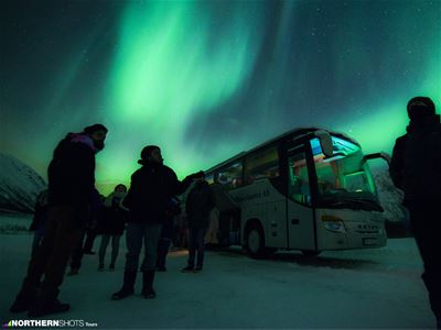 Guests outside the bus with northern lights in the background