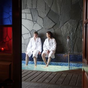 Two persons are sitting on the edge of the indoor pool. 