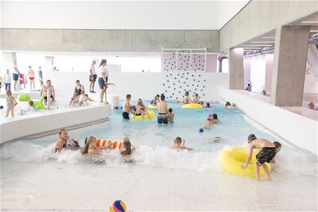 People of all ages enjoying a bright indoor swimming pool with a climbing wall