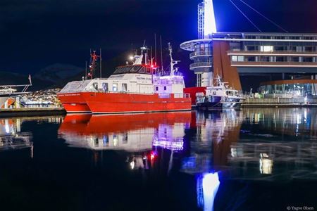 En rød båt ved kai i Tromsø havn på kveldstid.