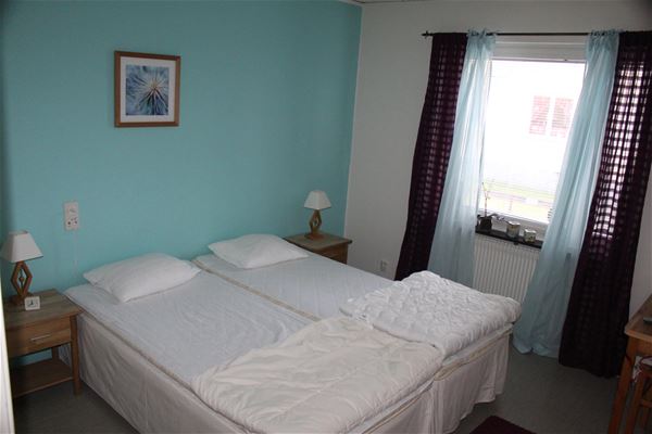 A double bed in a bedroom with light blue walls and light blue and black curtains.  