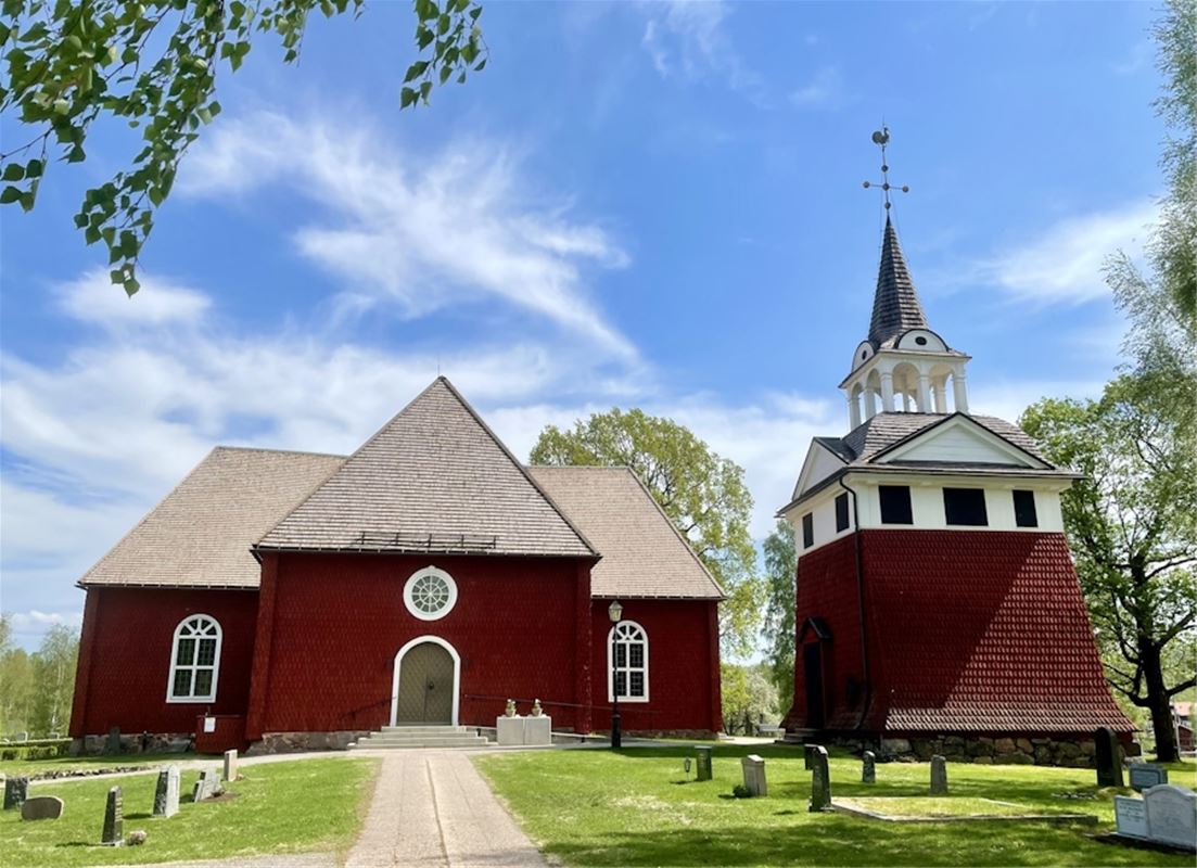 Sundborns kyrka, exteriörbild, röd träkyrka med grön dörr, gång fram till kyrkan, klockstapel till höger.
