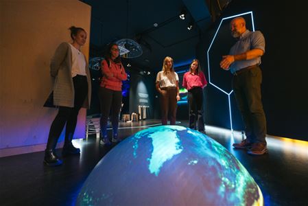 Five people around a digital globe in a dark exhibition room.