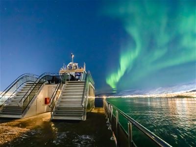 Picture of the boat in the sea with Northern Lights above