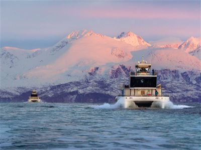 Brim Explorer cruising through Arctic waters with snow-covered mountains around Tromsø in the background.