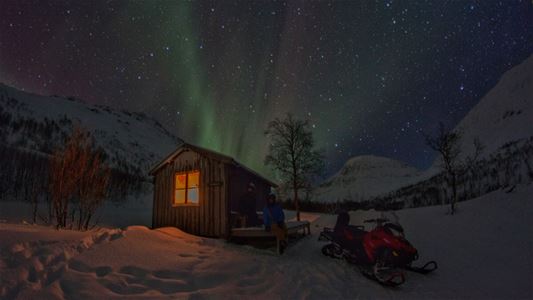 En hytte og snøskuterne under nordlyset
