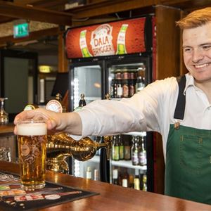 A person in apron holding a glass of beer.