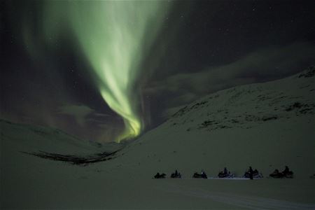 6 snow scooters drive under the Northern Lights amidst the mountains in Camp Tamok
