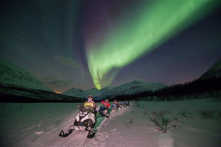 Snow scooters driving in a line under the Northern Lights at Camp tamok, Norway
