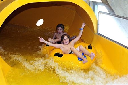 Two children come out of the tunnel in the water slide, they are lying on large swimming rings.