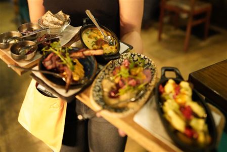 Tray with several small dishes, including flatbread, soup, grilled meat, salad and a pasta dish, in an indoor restaurant setting.